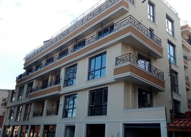 Modern multi-story apartment building with beige facade and decorative wrought iron balconies.