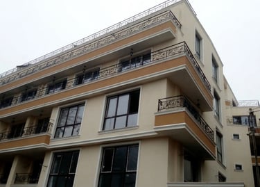 Modern multi-story apartment building with beige facade and decorative wrought iron balconies.