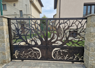 Custom laser-cut decorative metal driveway gate featuring a branching tree design and stone pillars.