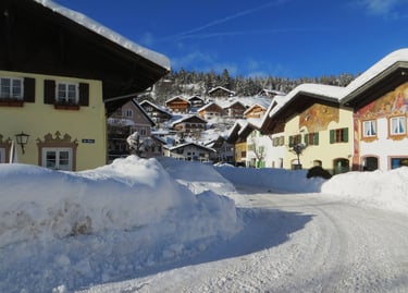 Snow-covered street in a Bavarian village with traditional alpine houses under a clear blue sky.