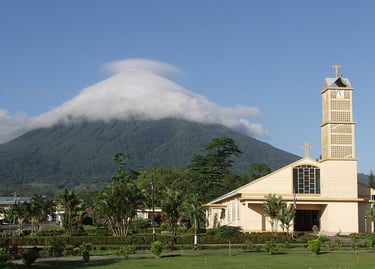 A scenic view of a yellow church with a clock tower and a volcano capped by clouds in Costa Rica.