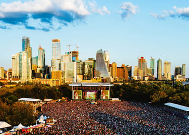 Crowded outdoor music festival at Austin City Limits with the downtown skyline at sunset.