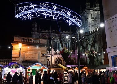 Festive Bath Christmas Market with illuminated star lights in front of Bath Abbey at night.