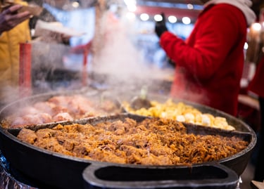 Steaming hot pans of traditional street food including stewed meat and potatoes at a festive European Christmas market.