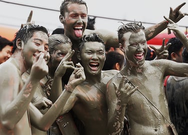 Smiling people covered in mud celebrating at a messy outdoor mud festival event.