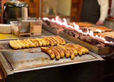 German bratwurst sausages grilling on a flat top stove next to an open charcoal flame at a food stall.