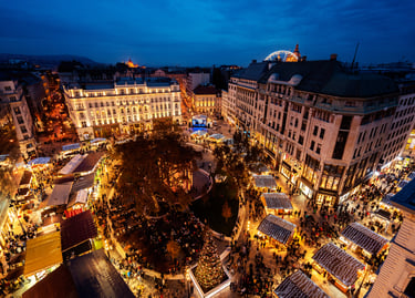 Aerial view of the Budapest Christmas Market at night with festive lights, stalls, and a Ferris wheel.