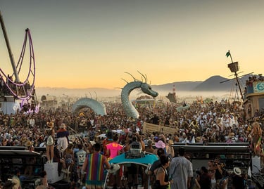 Crowd gathers around a sea serpent art installation and desert art cars at Burning Man festival.