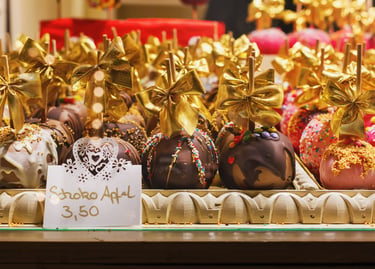 Gourmet chocolate covered apples with gold bows and colorful sprinkles at a European Christmas market stall.