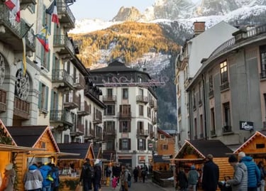 Crowded Christmas market in Chamonix, France, with wooden stalls and snow-capped Alpine mountains in the background.