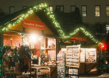 A festive outdoor Christmas market stall at night decorated with string lights and selling artisan gifts.