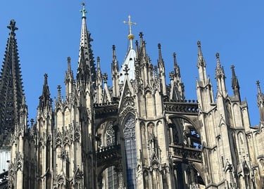 Intricate Gothic architecture and stone spires of the Cologne Cathedral under a clear blue sky.