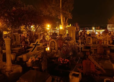 Night view of a Mexican cemetery during Day of the Dead with lit gravestones and flowers.