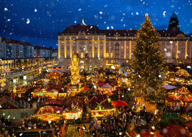 Festive Christmas market in Dresden at night with falling snow, glowing stalls, and a large decorated tree.