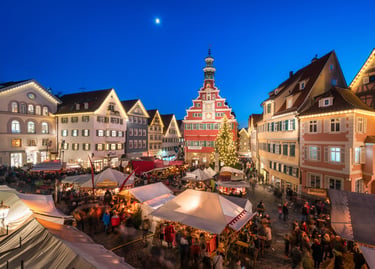 Esslingen Christmas market stalls illuminated at night with historical architecture and moonlit sky.