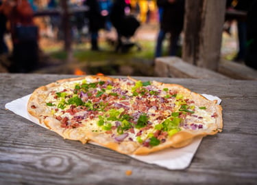 Traditional German Flammkuchen with bacon, onions, and scallions on a rustic wooden table.