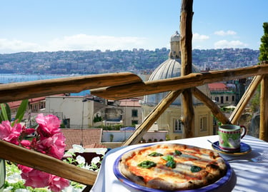 Fresh Neapolitan pizza on a balcony overlooking the city of Naples and the Mediterranean Sea.