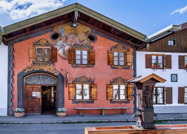 Traditional Bavarian house in Oberammergau with Lüftlmalerei frescoes and a wooden fountain.
