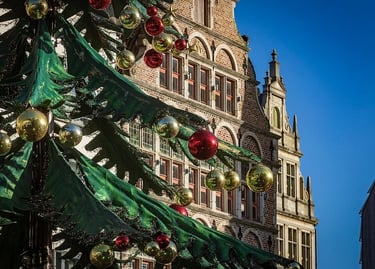 A decorated Christmas tree with red and gold ornaments in front of a historic European brick building.