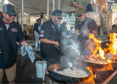 Professional chefs cooking seafood over an open flame grill at a busy outdoor food festival.