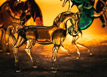 Elegant amber-colored hand-blown glass horse figurine standing on a dark surface with a glowing background.