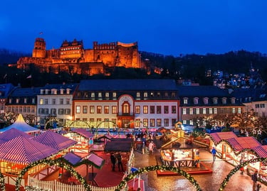 Illuminated Heidelberg Christmas market stalls at night with the historic Heidelberg Castle in the background.
