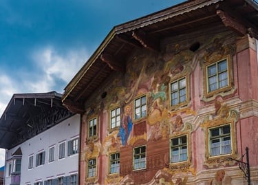 Bavarian house with traditional Lüftlmalerei frescoes and religious murals under a blue sky.