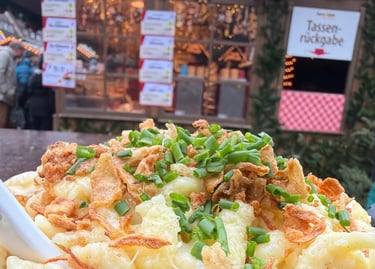 Cheesy German Kaesespaetzle topped with fried onions and chives at a festive Christmas market stall.