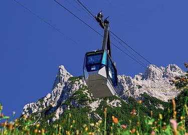 Cable car gondola ascending towards rugged mountain peaks in the Alps under a clear blue sky.