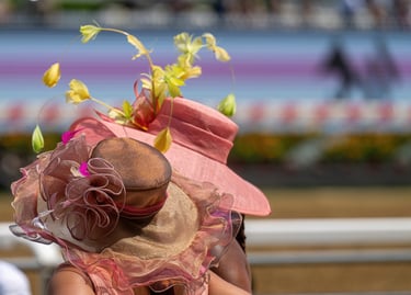 Elegant women wearing decorative Kentucky Derby style hats at a horse racing track.