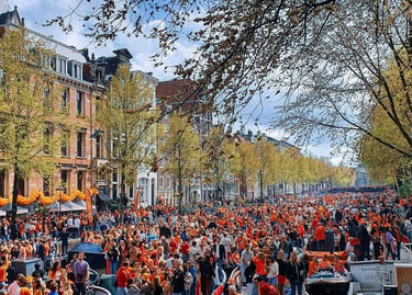 Crowds in orange clothing celebrate King's Day along the historic Amsterdam canals and city streets.