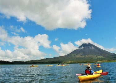 Tourists in yellow kayaks paddle on Lake Arenal with the Arenal Volcano in the background.