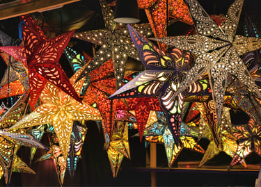 A vibrant display of illuminated paper star lanterns with intricate cutouts hanging at a Christmas market.