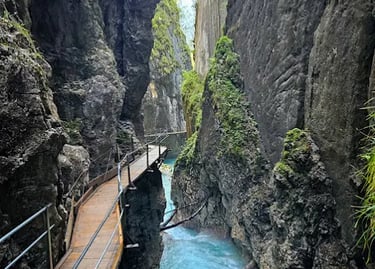 A narrow wooden walkway along steep rock walls above a turquoise river in a mountain gorge.
