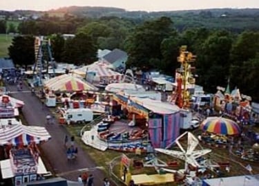 Aerial view of a colorful outdoor carnival with amusement park rides, game booths, and striped tents.