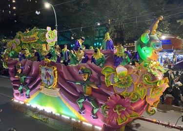 A colorful Mardi Gras float with masked riders and jester decorations in a New Orleans parade.