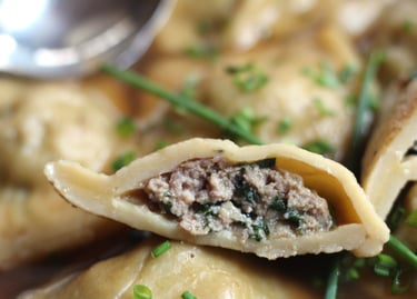 A sliced German Maultasche dumpling filled with minced meat and spinach, garnished with fresh chives.