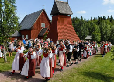 Traditional Swedish musicians in folk costumes playing violins outside a historic red wooden church.
