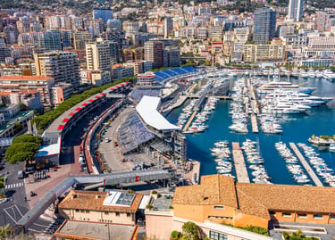 Aerial view of Port Hercules in Monaco featuring luxury yachts, the Formula 1 Grand Prix circuit, and city skyline.
