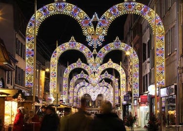 Illuminated Christmas market street with festive light arches and holiday shoppers at night.