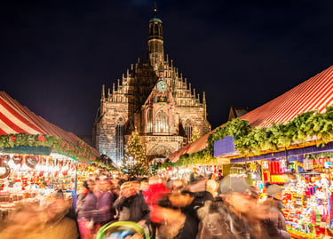 Crowded Nuremberg Christmas Market at night with festive stalls and the Church of Our Lady background.