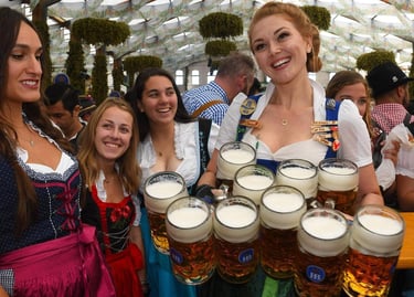 Smiling waitress in a traditional dirndl carrying several large mugs of beer at Oktoberfest.