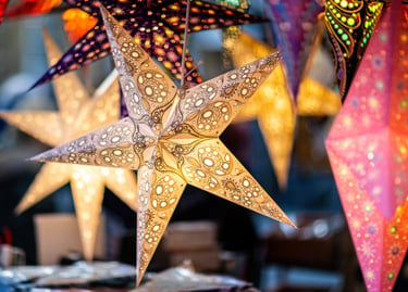 Hanging paper star lanterns with intricate patterns glowing at a Christmas market.