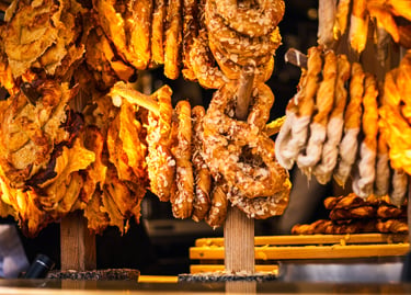 Freshly baked German pretzels and sweet pastries with almond flakes on wooden display stands at a market.