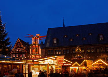 Crowded German Christmas market at night with festive lights, food stalls, and a traditional pyramid.
