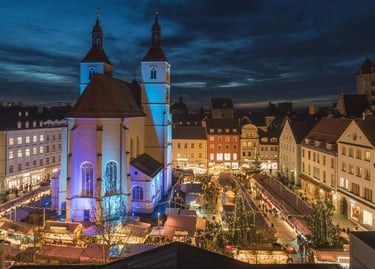 Elevated view of a traditional German Christmas market at night with festive lights and a historic church.