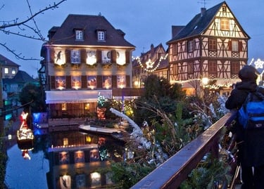 Scenic Colmar canal at dusk with festive Christmas lights and historic half-timbered houses.