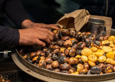 A street vendor's hands sorting hot roasted chestnuts in a large pan at a winter market.