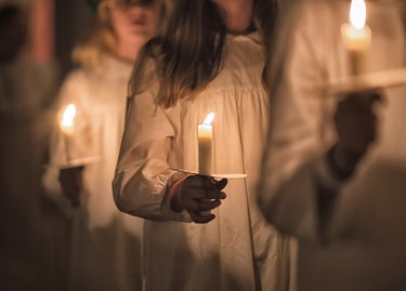 Children in white robes holding glowing candles during a traditional Saint Lucia Day procession.
