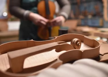 Handcrafted wooden violin body in a luthier workshop with a violin maker working in the background.